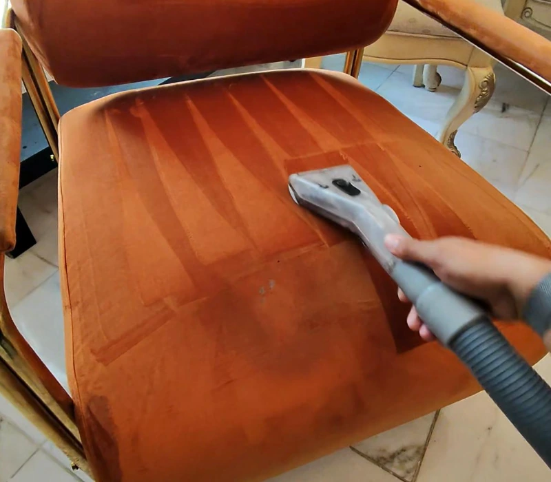 Upholstery tool steam cleaning an orange velvet chair seat