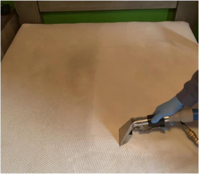 Upholstery tool cleaning a light fabric mattress, showing the clean half