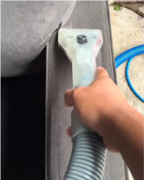 Hand guiding an upholstery wand over a gray couch armrest