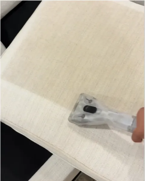 Upholstery tool steam cleaning a cream chair cushion