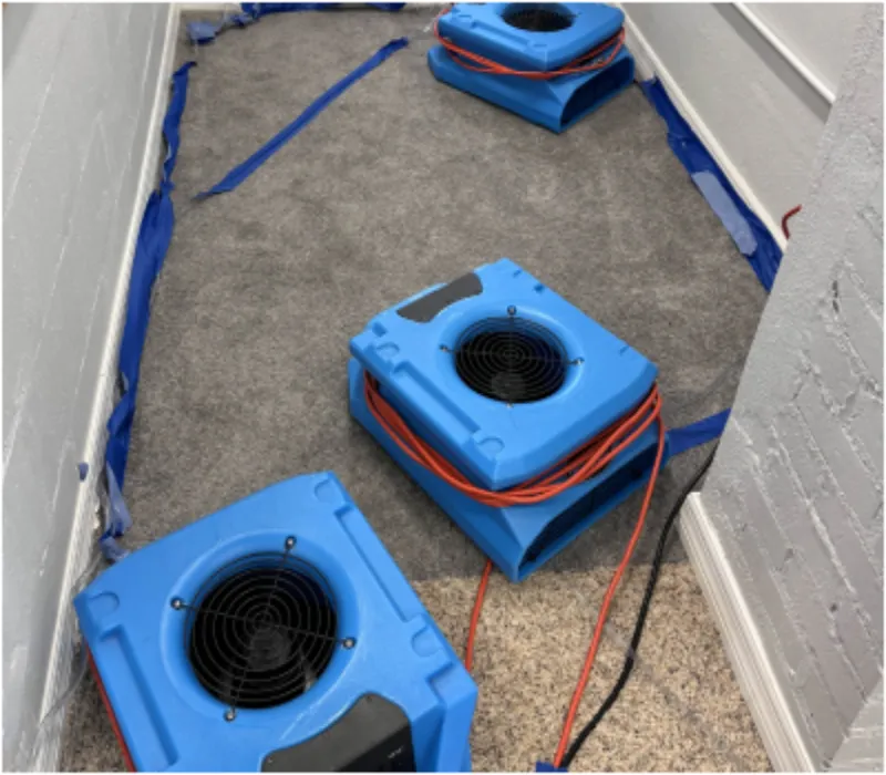Industrial air movers drying a water-damaged carpet in a hallway